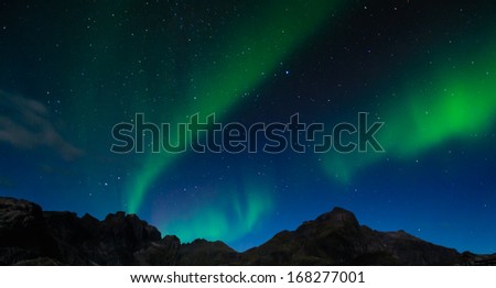 Northern lights shine bright and beautiful above sharp peaks and lakes of Lofoten mountains, Norway