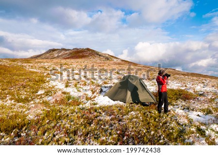 Woman photographer and hiker taking picture of beautiful evening light in mountains in front of her tent