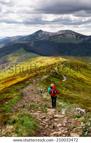 Women hiker with heavy backpack is climbing the ridge of Bieszczady mountains during her wild expedition through Poland and Slovakia