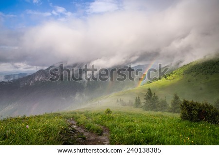 Mountain ridge covered in low clouds with beautiful rainbow right after quick summer storm, fresh nature