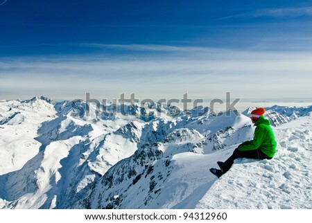 Skier having a break, sitting on the edge and being overwhelmed by beauty of high mountains, Austrian Alps below