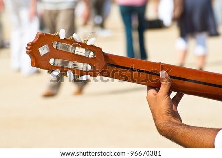 Young artist plays guitar outside in the park full of people