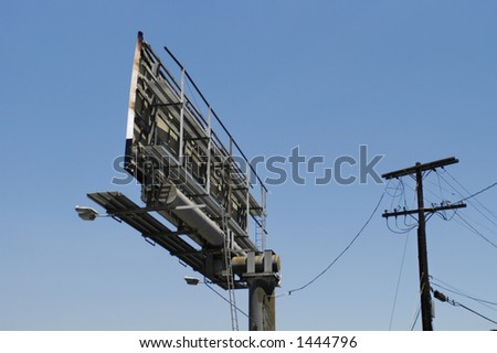 A the rear of an elevated billboard flanked by a utility pole against a blue sky