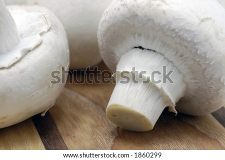A close-up of large closed cup mushrooms on a kitchen chopping board