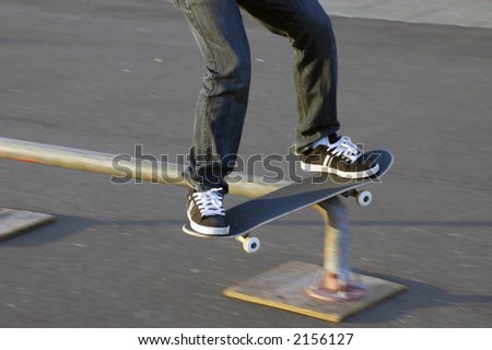 Lower body of youth in motion, riding skateboard on rail (motion blur)