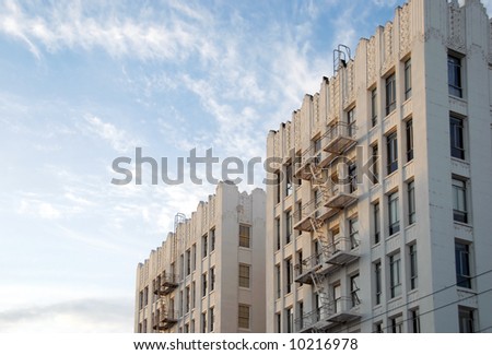 Weathered white art deco apartment buildings lit by low sun with blue sky and clouds