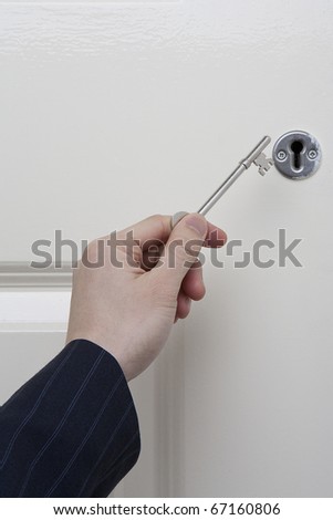 Key opening a door. Businessman hand holding door key
