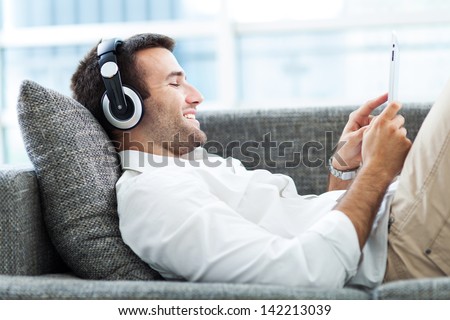 Man On Sofa With Headphones And Digital Tablet