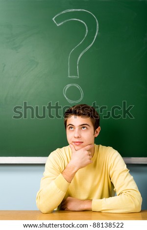 Man sitting next to question mark on blackboard