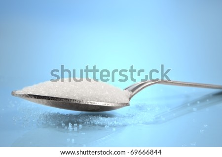 Close and low level capturing a tea spoon with sugar granules against a blue background.