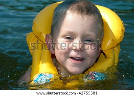 Close-up portrait of a smiling boy in a yellow life jacket is swimming in the river