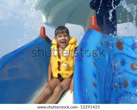 Young boy in yellow life jacket sitting on colorful water slide in aquapark