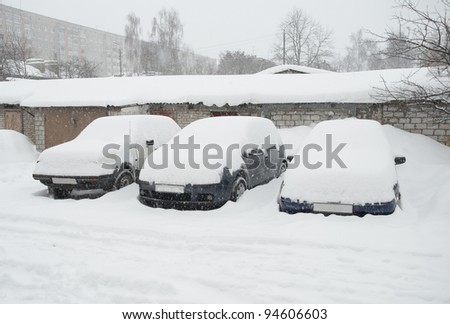 Three cars covered with snow in the winter blizzard on the street of city