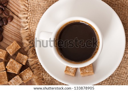 closeup view of a cup of coffee, brown sugar and coffee beans