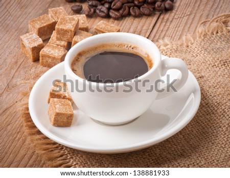 closeup view of a cup of coffee, brown sugar and coffee beans