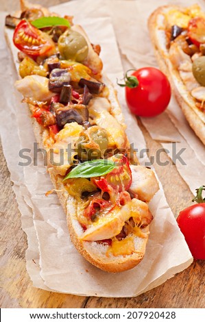 Big sandwich with roasted vegetables (zucchini, eggplant, tomatoes) and chicken with cheese and basil on old wooden background