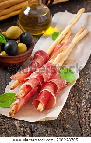 Grissini bread sticks with ham, olives, basil on old wooden background