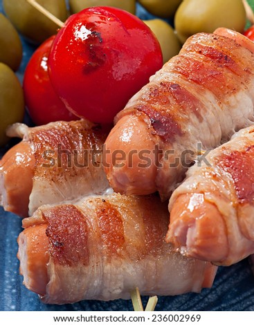 Grilled sausages wrapped in strips of bacon with tomatoes and sage leaves