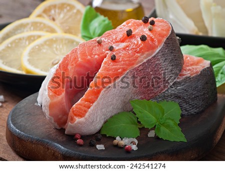 Fresh and raw steaks trout on a wooden cutting board with sliced lemon, basil and pepper