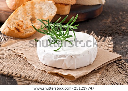 Camembert cheese and a sprig of rosemary on a wooden table