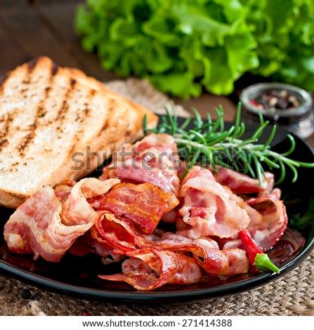 Fried bacon and toast on a black plate on a wooden background