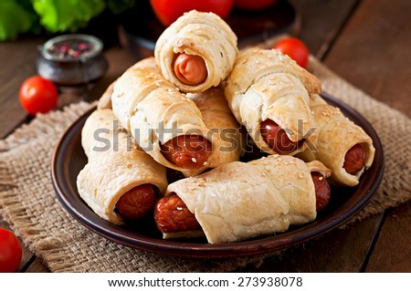 Sausage in the dough sprinkled with sesame seeds on a wooden background in rustic style