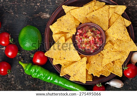 Mexican nacho chips and salsa dip in bowl on wooden background. Top view.