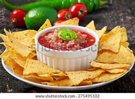 Mexican nacho chips and salsa dip in white bowl on wooden background