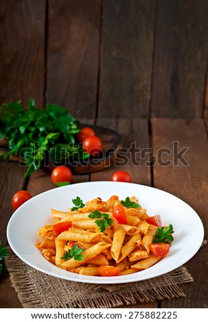 Penne pasta in tomato sauce with chicken, tomatoes decorated with parsley on a wooden background