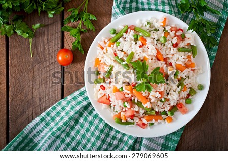 Appetizing healthy rice with vegetables in white plate on a wooden background. Selective focus. Top view.