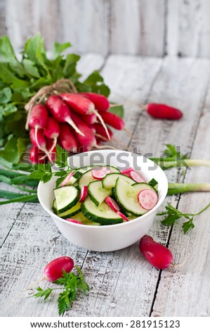 Fresh salad of cucumbers and radishes in a white bowl on the old wooden background