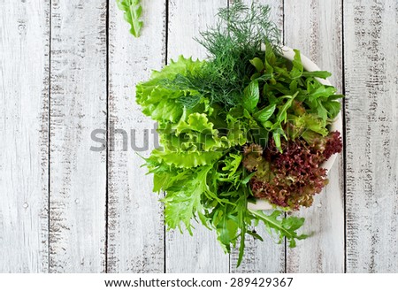 Variety fresh organic herbs (lettuce, arugula, dill, mint, red lettuce) on wooden background in rustic style. Top view