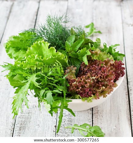 Variety fresh organic herbs (lettuce, arugula, dill, mint, red lettuce) on wooden background in rustic style.