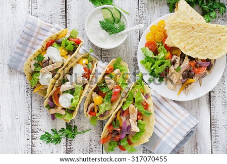 Mexican tacos with chicken, bell peppers, black beans and fresh vegetables and tartar sauce. Top view