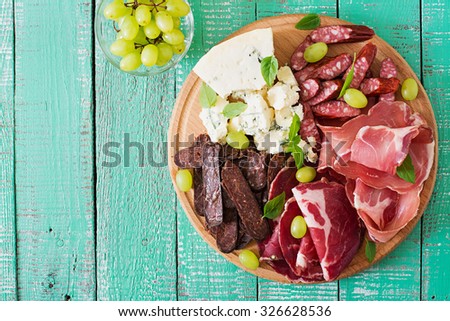 Antipasto catering platter with bacon, jerky, sausage, blue cheese and grapes on a wooden background. Top view