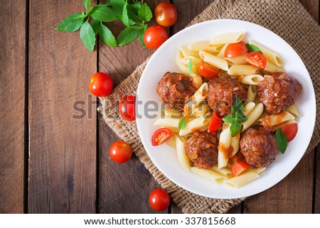 Penne pasta with meatballs in tomato sauce in a white bowl. Top view