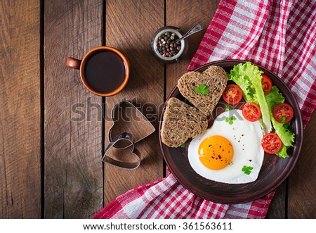Breakfast on Valentine\'s Day - fried eggs and bread in the shape of a heart and fresh vegetables. Top view