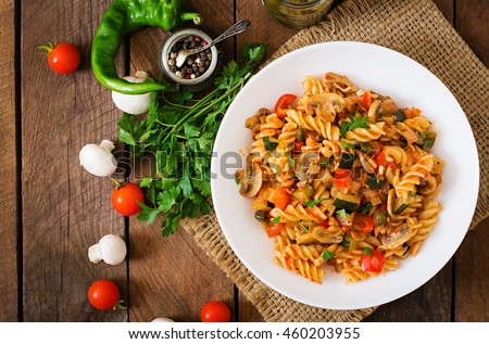 Vegetarian Vegetable pasta Fusilli  with zucchini, mushrooms and capers in white bowl on wooden table. Top view