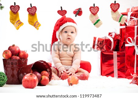 Cute little girl in Santa hat sitting on floor among gifts and fruit