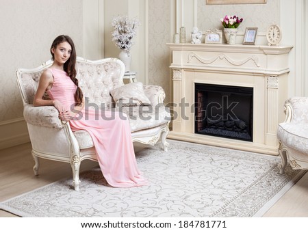 Young girl in elegant pink dress sitting on couch in luxury interior