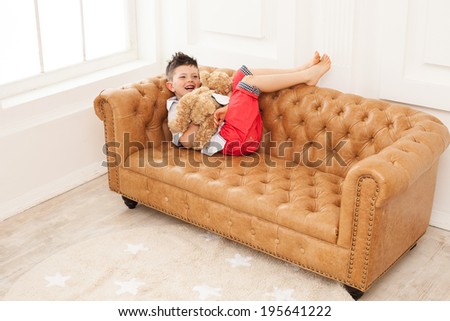 Young boy holding toy and laughing while lying down on sofa at home