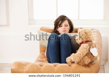 Young girl reading book while sitting on couch at home
