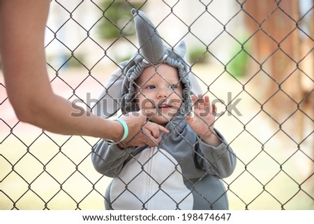 Cute little boy dressed in elephant costume playing behind the net, cropped view of mother in the foreground