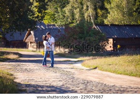 Young couple in Ukrainian style clothing kissing while standing on road in old village