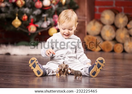 Cheerful little boy playing with his toy animals by Christmas tree