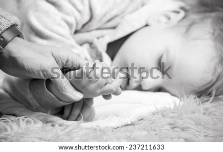 Closeup view of mother holding son\'s hand while he is sleeping