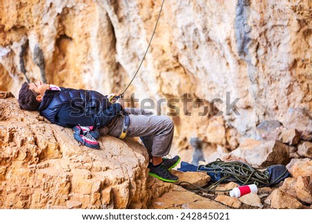 Young man lying on stone and watching leading rock climber while belaying