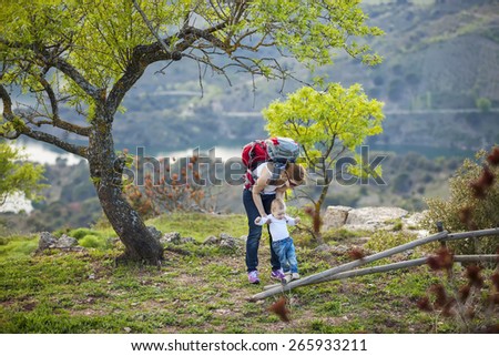 Young woman supporting son while he is making first steps outdoors