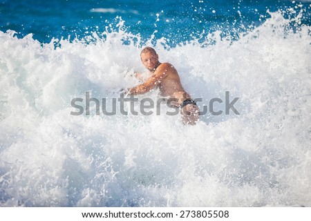 Young man bathing in storming sea, high wave just washed his over, water in focus