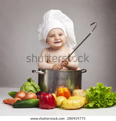 Joyful little boy in chef\'s hat sitting in large casserole and holding ladle
